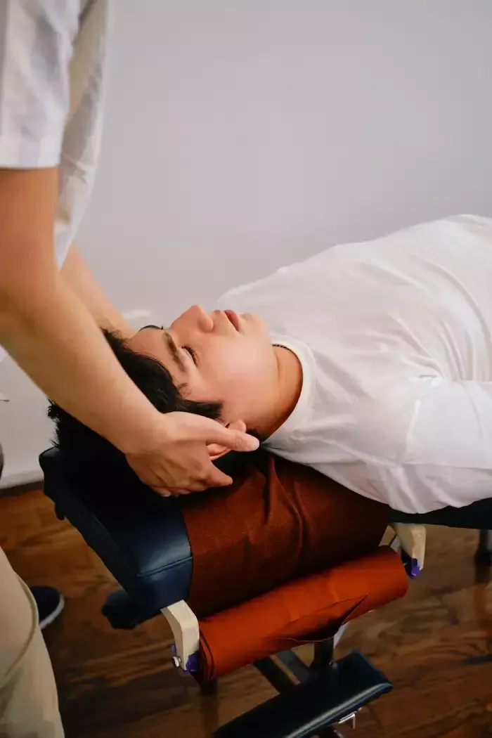 Dr. Leo Quan assessing a patient’s neck with hands supporting the head while the patient lies face up on a chiropractic table.