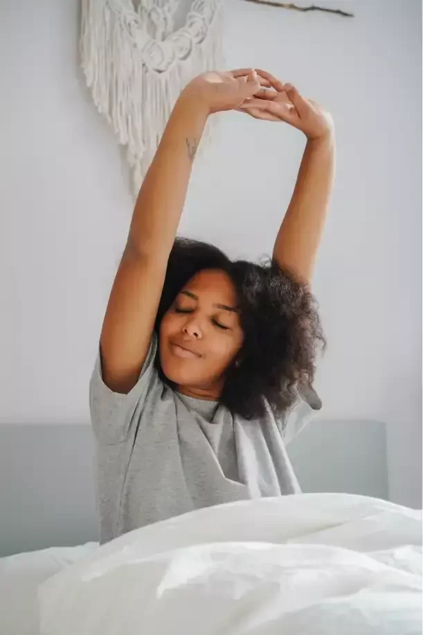 Woman sitting up in bed and stretching both arms overhead after waking.