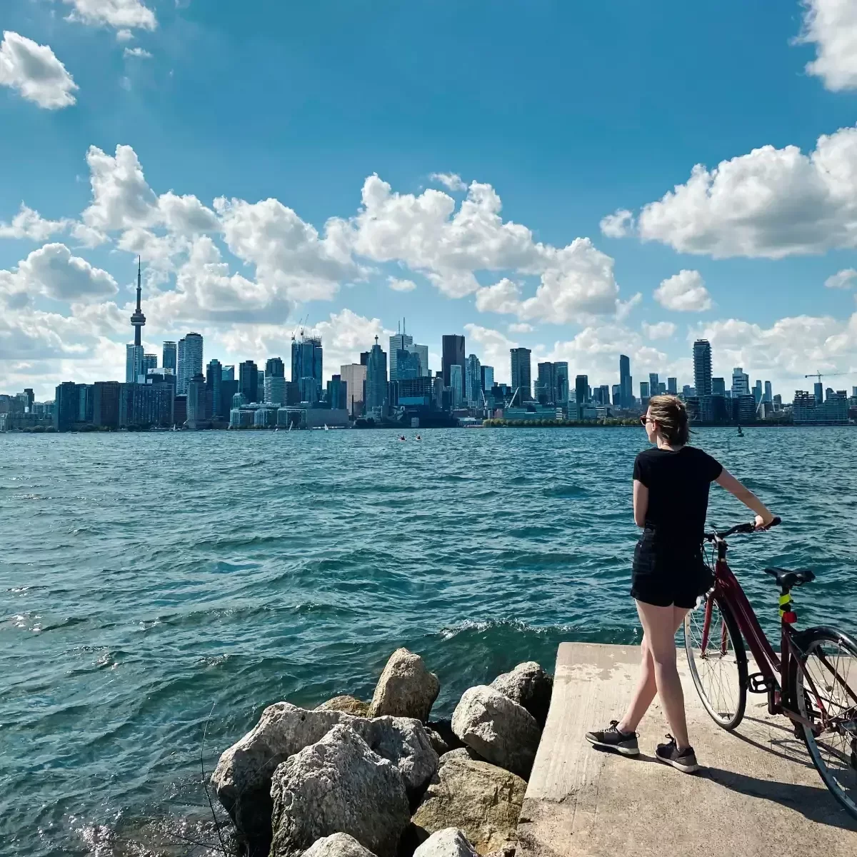 Toronto skyline and CN Tower viewed across Lake Ontario with a cyclist in the foreground.