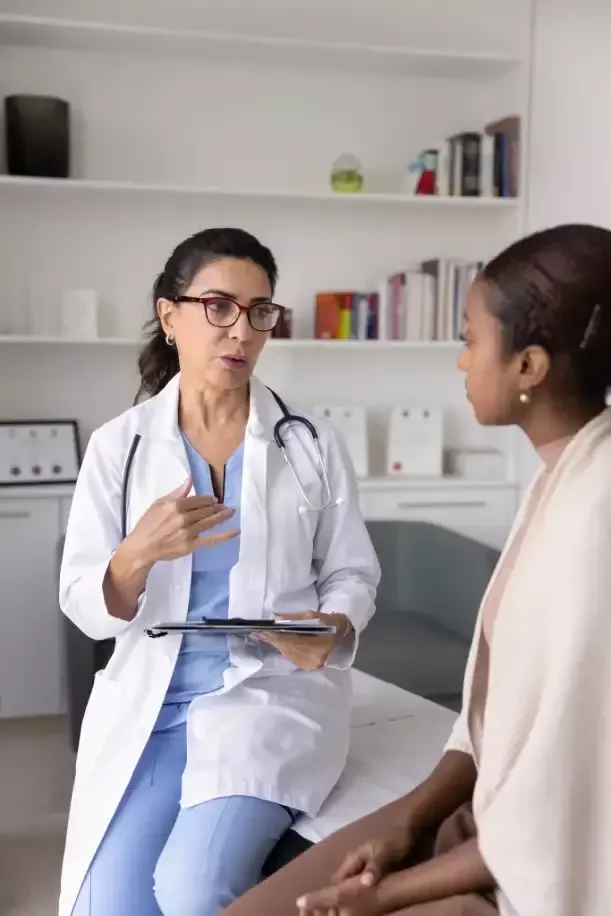 Doctor holding a tablet and discussing health concerns with a patient seated in an examination room.