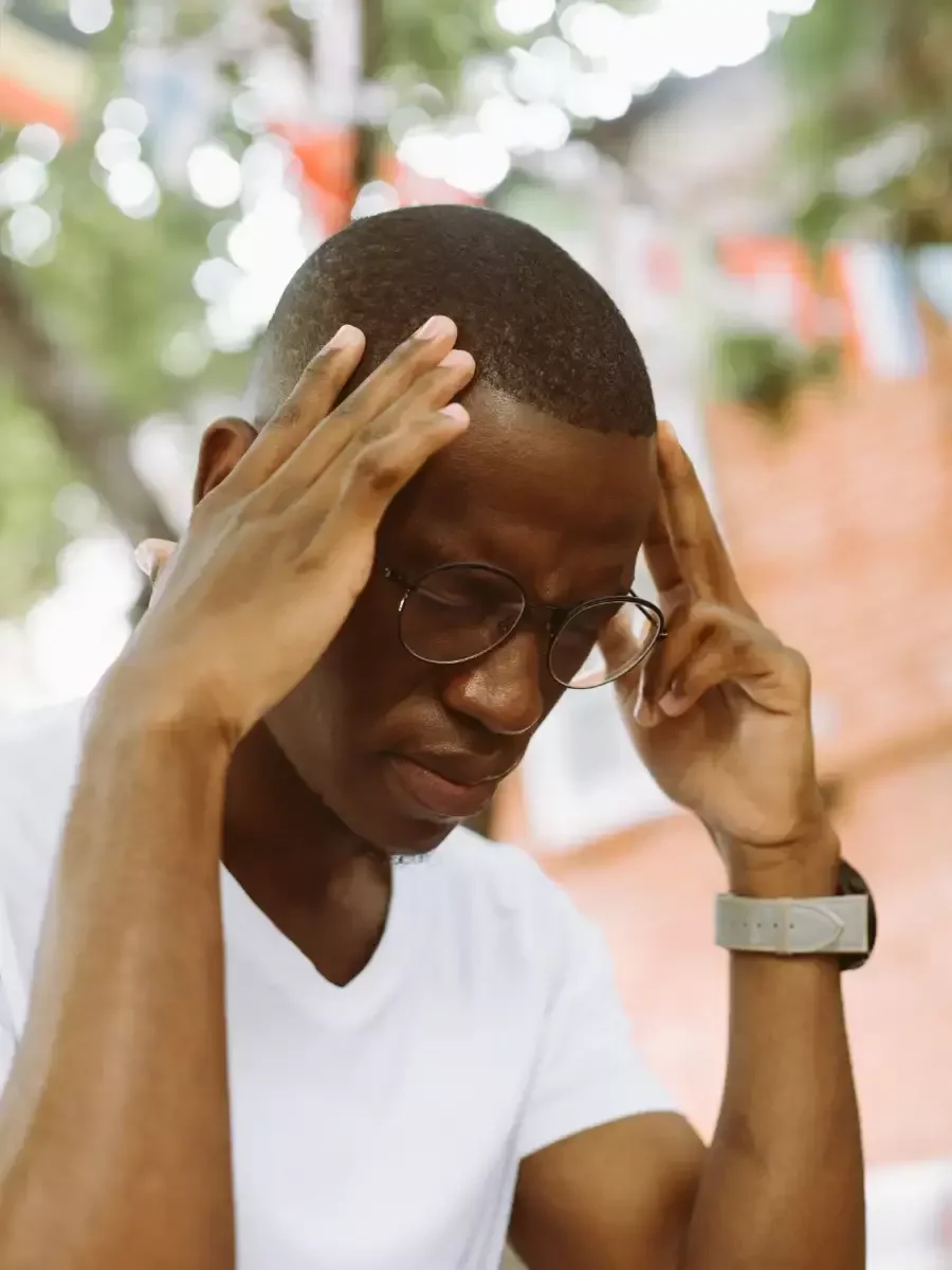 Man wearing glasses holding his temples with eyes closed, appearing to have a headache.