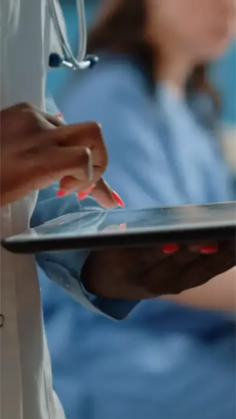 Healthcare professional using a tablet, with another clinician in blue scrubs in the background.
