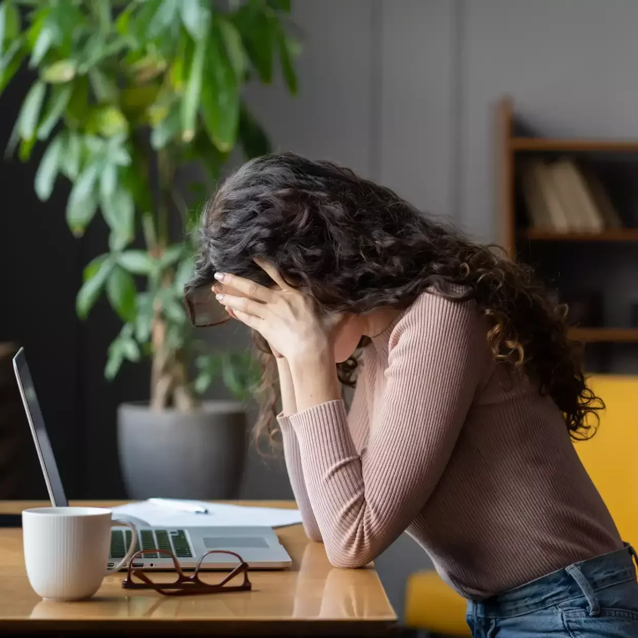 Office worker sitting at a laptop with her face in her hands, experiencing headache and fatigue.